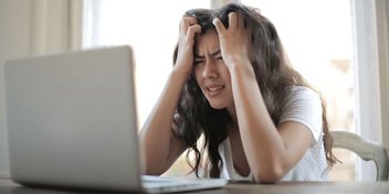 Eine verzweifelte Frau sitzt vor ihrem Computer und hält sich die Hände an den Kopf.