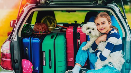 Ein Kind sitzt mit Gepäck und Hund im Auto