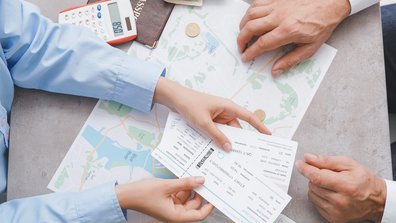 Das Foto zeigt eine Draufsicht des Tisches eines Reisebüros, auf dem eine Karte sowie Karten zu sehen sind. Das Foto illustriert einen Artikel zum Thema Kartenkauf der Olympischen Spiele 2024.