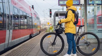 Ein Mann steht mit seinem Fahrrad am Bahngleis und steigt in einen Zug ein.
