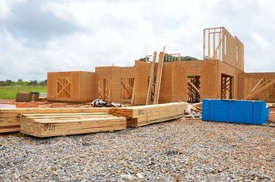 Grundgerüst eines Hauses auf einer Baustelle. Davor steht Baumaterial aus Holz.