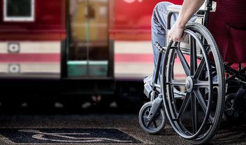 Eine Person sitzt in einem Rollstuhl am Bahngleis und wartet auf den Zug.