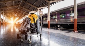 Ein vollbeladener Gepäckwagen mit Koffern steht an einem Bahnsteig. Im Hintergrund steht ein Zug.