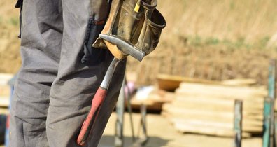 Ein Handwerker auf einer Baustelle. An seiner Hose hängt ein Hammer.