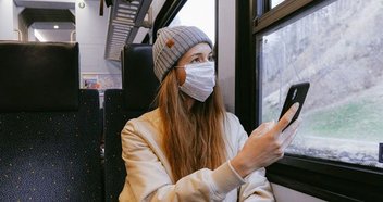Bahn fahren während Corona: Eine junge Frau sitzt mit einer Maske in einem Zug.