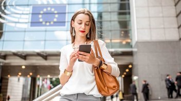 Das Bild zeigt eine junge Frau, die vor dem Europaparlament steht. Es bebildert einen Artikel zu den Neuerungen der EU in Sachen Verbraucherschutz 2024.