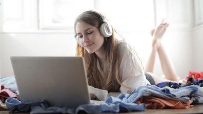 Eine junge Frau liegt auf ihrem Bett und streamt einen Film über einen Laptop.